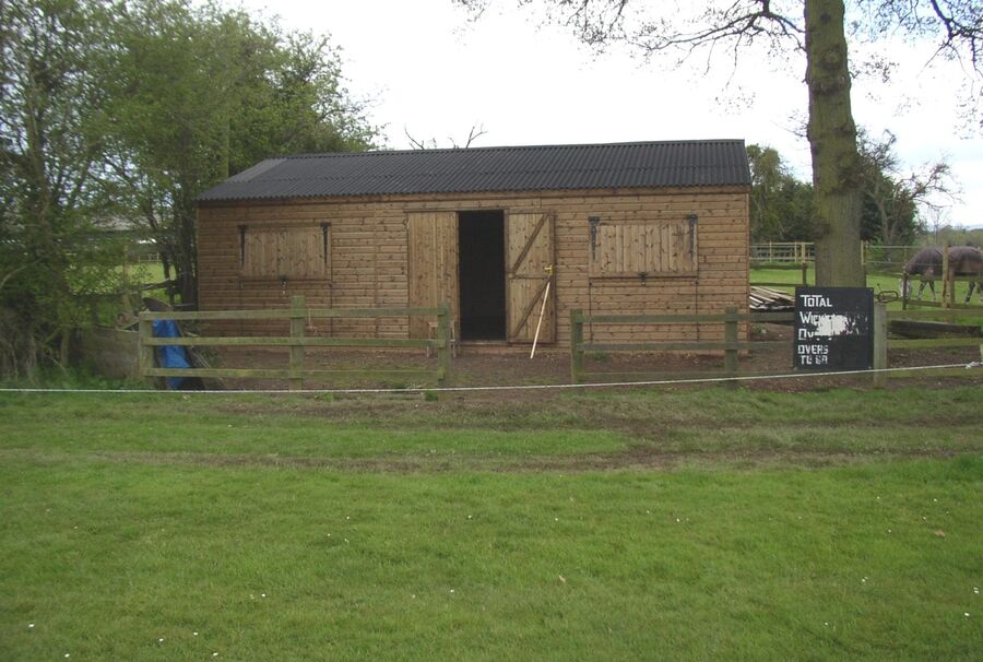 Timber cricket pavilion behind a post and rail fence
